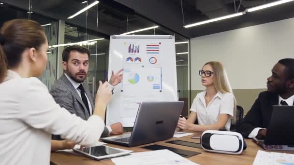 Guapo hombre de negocios barbudo confiado entrenador explicando a su grupo multirracial de negocios el valor del gráfico utilizando la presentación de rotafolio — Vídeo de stock