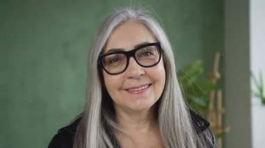 Pretty smiling stylish retired woman with gray hair wearing glasses and looking at camera with happy face