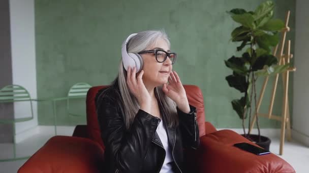 Портрет красивой моды 60-летней крутой женщины с седыми волосами, которая слушает музыку в наушниках и танцует руками — стоковое видео
