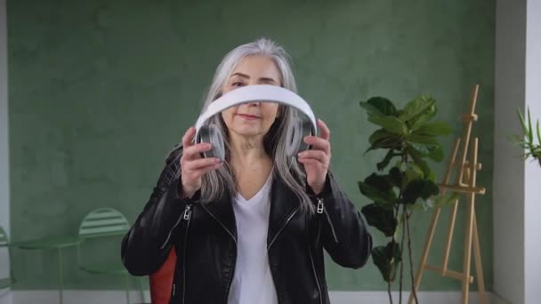 Porträtt av attraktiv hög-pigg snygg pensionerad kvinna som sätter på hörlurar och tittar på kameran med vackra leende — Stockvideo
