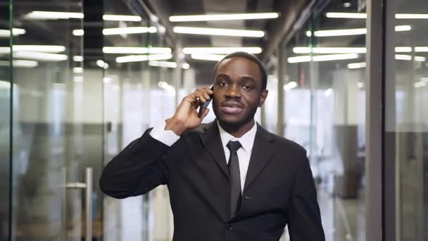 Attractive smiling black-skinned businessman having business conversation with partner while walking through the office hall — Αρχείο Βίντεο