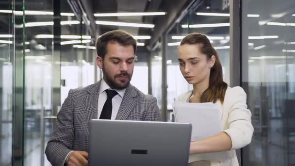 Vue de face de beaux gens d'affaires concentrés expérimentés qui travaillent sur ordinateur portable, debout dans le couloir de bureau moderne — Video