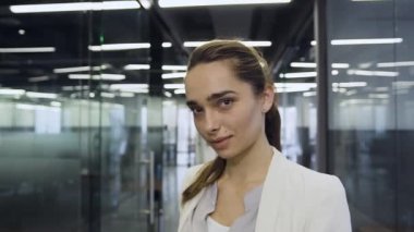 Front view of charming smiling young business lady which posing on camera in long office hall while using tablet pc