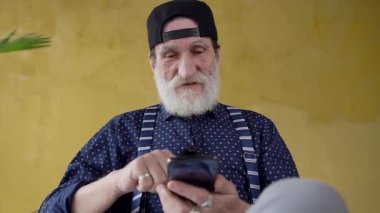 Slow motion of happy good-looking bearded stylish man in youthful cap which using his smartphone to search needed information