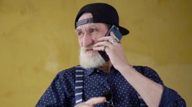 Front view of happy smiling modern bearded senior man in cap which having phone conversation with friend