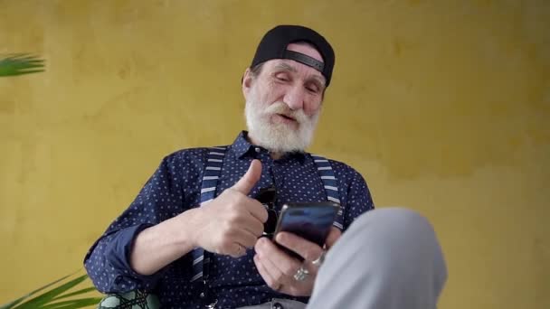 Happy respected cool bearded 70-aged grandfather in stylish cap is satisfied the find results on mobile screen — Wideo stockowe