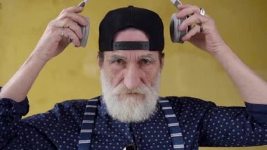 Portrait of smiling calm respected mature bearded man in black cap which putting on headphones and looking at camera