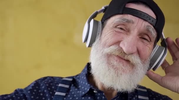 Primer plano de alegre hombre barbudo satisfecho con estilo en los auriculares que escuchan canciones modernas — Vídeos de Stock