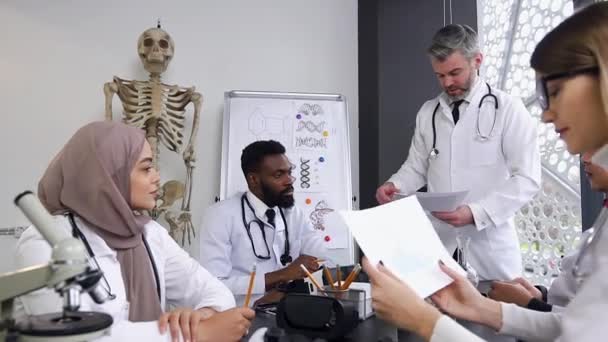 Squadra di medici misti che lavorano con documenti di lavoro durante la riunione mentre discutono qualcosa presso lo studio medico — Video Stock