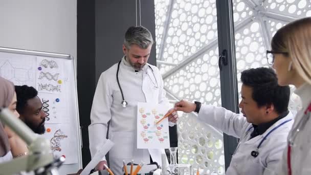 Caucasian male doctor conducts meeting of presentation with mixed race interns, explains something about the history illnesses and health of patients at hospital — Αρχείο Βίντεο