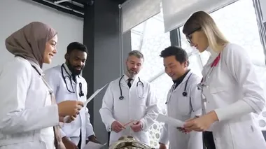 Portrait of professor and young medical interns of mixed race in medical clothing studying together human skeleton anatomy at lectures of surgery in light office in hospital