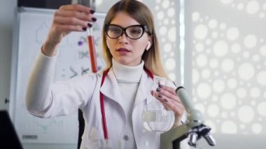Portrait of serious female doctor in glasses wich uses test tubes with liguid and doing medical researchh