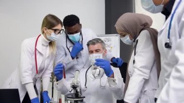 Adult male researcher and young multiracial team of scientists are working at samples in test tubes during the experiment at lab