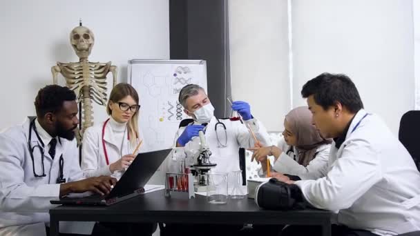 Grupo de cientistas internacionais que trabalham com produtos químicos usa microscópio e tubos de ensaio — Vídeo de Stock