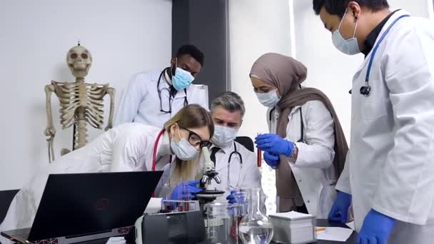 Diverse team of five research scientists working in laboratory of chemistry classroom with microscope and test tubes, analysing and vevelops test trial new generation drug data — 图库视频影像