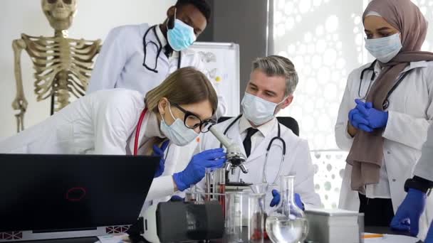 Oamenii de știință de sex feminin care caută în microscop și analizează studiile de testare a medicamentelor împreună cu care echipa multirasială de medici de știință care lucrează în laborator — Videoclip de stoc