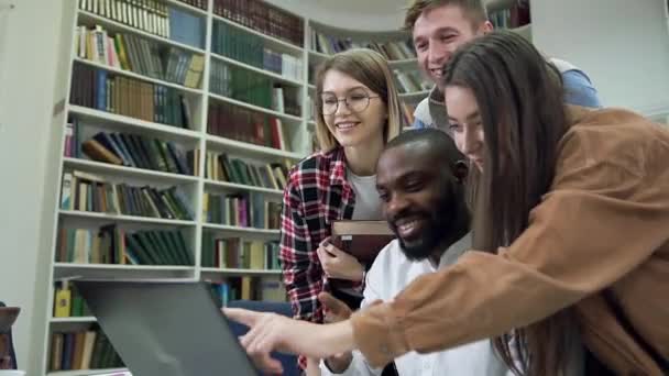 Привлекательные современные многонациональные друзья, работающие над домашней работой в библиотеке с помощью компьютера — стоковое видео