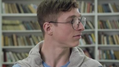 Close up of handsome smiling smart guy in glasses looking at camera in the library