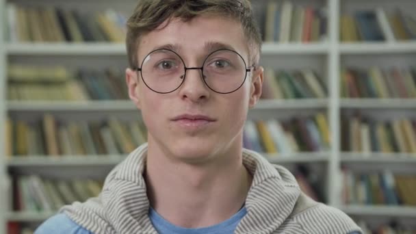 Movimento lento de bom aspecto puro sorrindo homem de 25 anos em óculos que posando na biblioteca — Vídeo de Stock