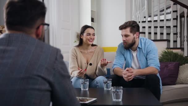Концепция офиса психолога, где привлекательная улыбающаяся женщина рассказывает мужчине-терапевту о проблемах в отношениях и ее грустном приятеле, слушающем — стоковое видео