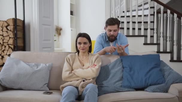 Enttäuschende junge, traurige Frau sitzt auf dem Sofa und hört zu, wie ihr bärtiger Mann Probleme im gemeinsamen Leben aufzählt — Stockvideo