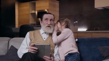 Çağdaş odada neşeli, şık, yaşlı büyükbabanın kulağına bir şeyler fısıldayan sevimli genç kızın ağır çekimleri.