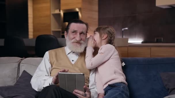 Detailní záběr krásné šťastné tennage dívka, která sedí spolu se svým pozorným pohledný 80-ti letý vousatý dědeček a sdílet s ním její tajemství na ucho — Stock video
