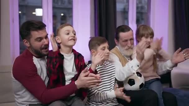 Opgewonden aantrekkelijke felle fans als drie kinderen, hun vader en grootvader die emotioneel kijken naar voetbalwedstrijd met klappende handen — Stockvideo