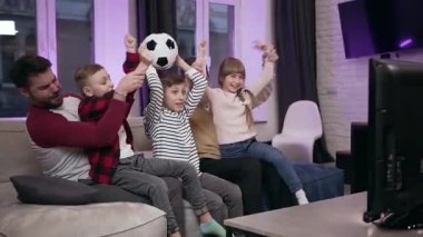 Evde kanepede oturan ve zaferi el kaldırarak kutlayan pozitif, çekici aile futbol fanatikleri.