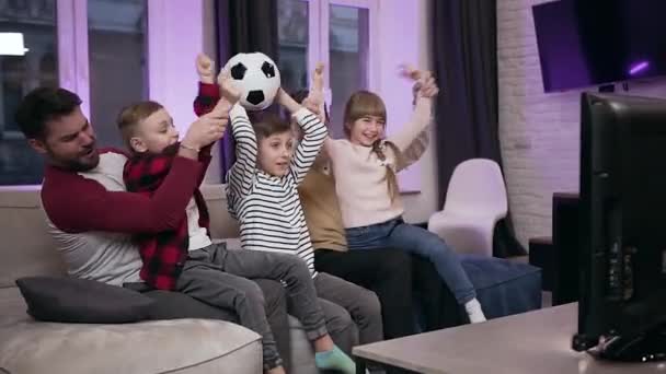 Izgatott pozitív vonzó családi labdarúgó rajongók ül a kanapén otthon, és ünnepli a győzelmet emelt kézzel — Stock videók