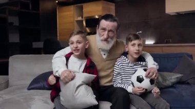 Heyecanlı, sakallı, olgun, duygusal torunları olan, TV 'deki futbol maçını gözden geçiren olgun büyükbabanın ön görüntüsü.
