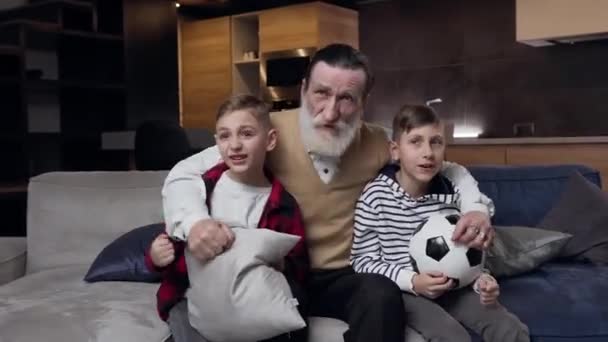Vooraanzicht van opgewonden aantrekkelijke bebaarde volwassen opa met emotionele tiener kleinzonen die herzien van de voetbalwedstrijd op tv — Stockvideo