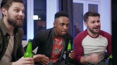 Close up of fierce attractive 30s mixed race male mates which celebrating victory of favourite football team during watching match on tv and enjoying beer