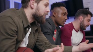Side view of attractive upset diverse group of men which watching sport game on tv and dissatisfied of bad game drinking beer