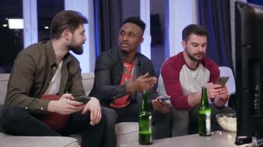 Portrait of attantive likable 30s diverse guys which get distracted on their phones during watching sport game on tv