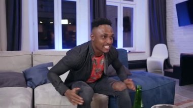 Emotional agitated black-skinned 30-aged guy cheering team and disappointing falling on the sofa with upset face