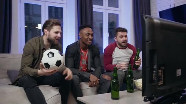 Atractivos jóvenes fanáticos del fútbol multirracial hombres sentados frente a la televisión y viendo el partido de fútbol — Vídeo de stock