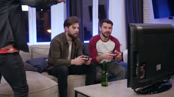 Два привлекательных современных взволнованных бородатых парня играют в видеоигры и дают пять своему третьему темнокожему другу, который приходит к ним — стоковое видео