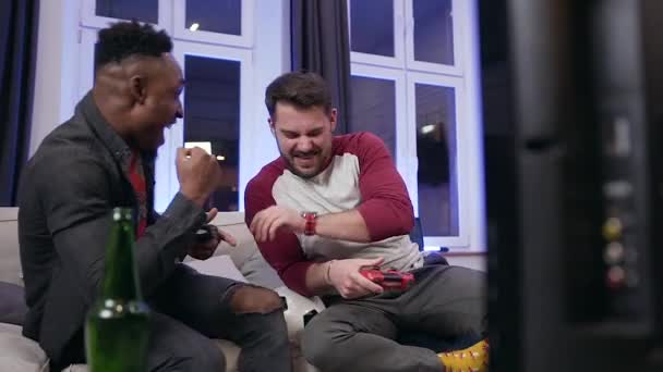 Alegre divertido atractivo mezclado raza dos amigos masculinos divertirse juntos durante jugar en los videojuegos en casa — Vídeos de Stock