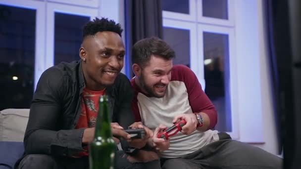 Close up of positive cheerful two 30s mixed race male friends which enjoying video games on tv using gamepads,one of them winning and another losing the game — ストック動画