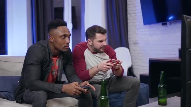 Concentrated good-looking modern diverse male mates sitting in front of tv and playing video games using gamepads — Stok video