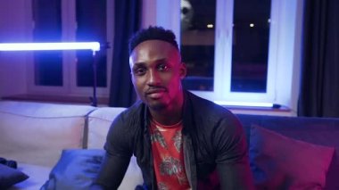 Front view of good-natured joyful modern stylish african american which putting earphones on his head and listening songs ,moving his body and hands in the beat of the music