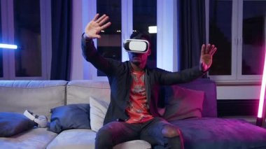 Attractive concentrated modern black-skinned guy in special 3d glasses moving hands on virtual screen sitting on the couch in his room