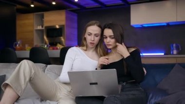 Çekici, mutlu 25 'li yaşlarda, ortak boş zamanlarını bilgisayar kullanarak, çağdaş oda stüdyosunda oturarak geçiren kadın arkadaşların ön görüntüsü.