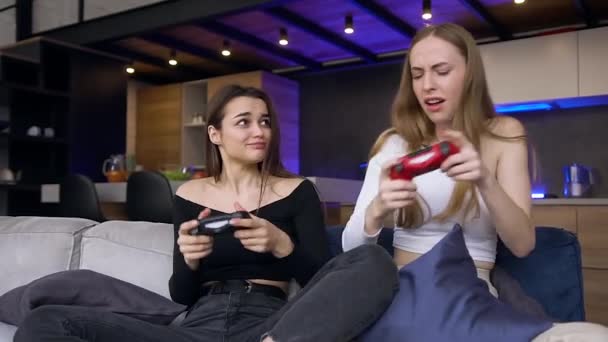 Забавно весело привлекательные две 25-летние женщины играют в видеоигры с помощью джойстиков, где одна празднует победу, другая проигрывает — стоковое видео