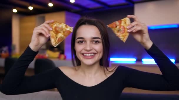 Encantador alegre jovem morena posando na câmera com sorriso de sorte enquanto segura em suas mãos duas fatias de pizza — Vídeo de Stock