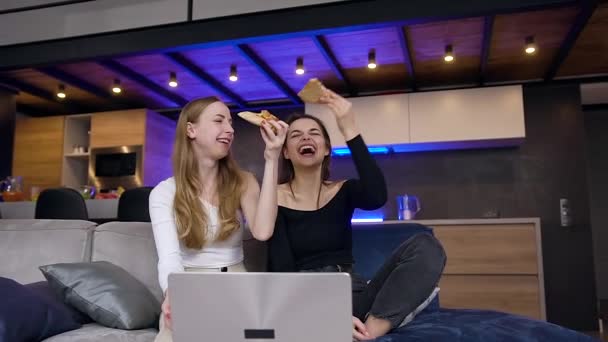 Веселые симпатичные счастливые молодые женщины весело вместе во время совместного досуга, где едят пиццу и смотреть программы на ноутбуке — стоковое видео