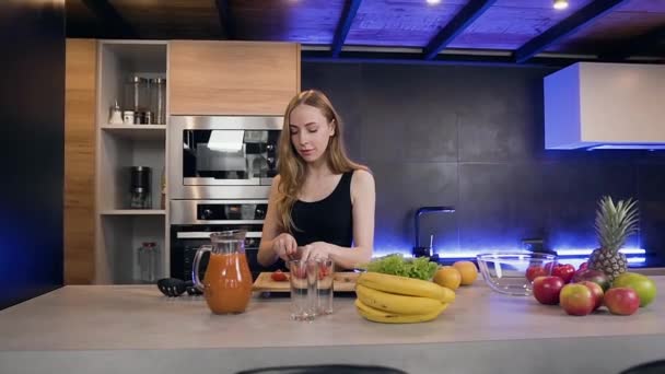 Charmante, zufriedene junge Frau schneidet rote Tomaten, um frischen Salat zuzubereiten und schaut beim Kochen mit einem netten Lächeln in die Kamera — Stockvideo