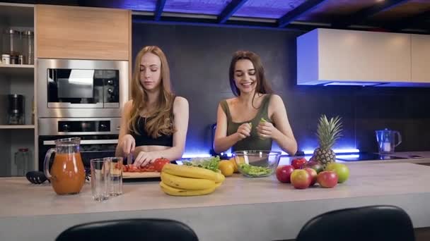 Primer plano de dos jóvenes encantadoras compañeras felices que se divierten en la cocina durante la preparación de una refrescante ensalada natural — Vídeo de stock