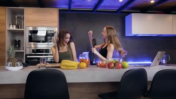 Gyönyörű pozitív érzelmek két fiatal nő tartja a kezükben konyha elemek táncolnak együtt a gyönyörűen megtervezett konyhában — Stock videók